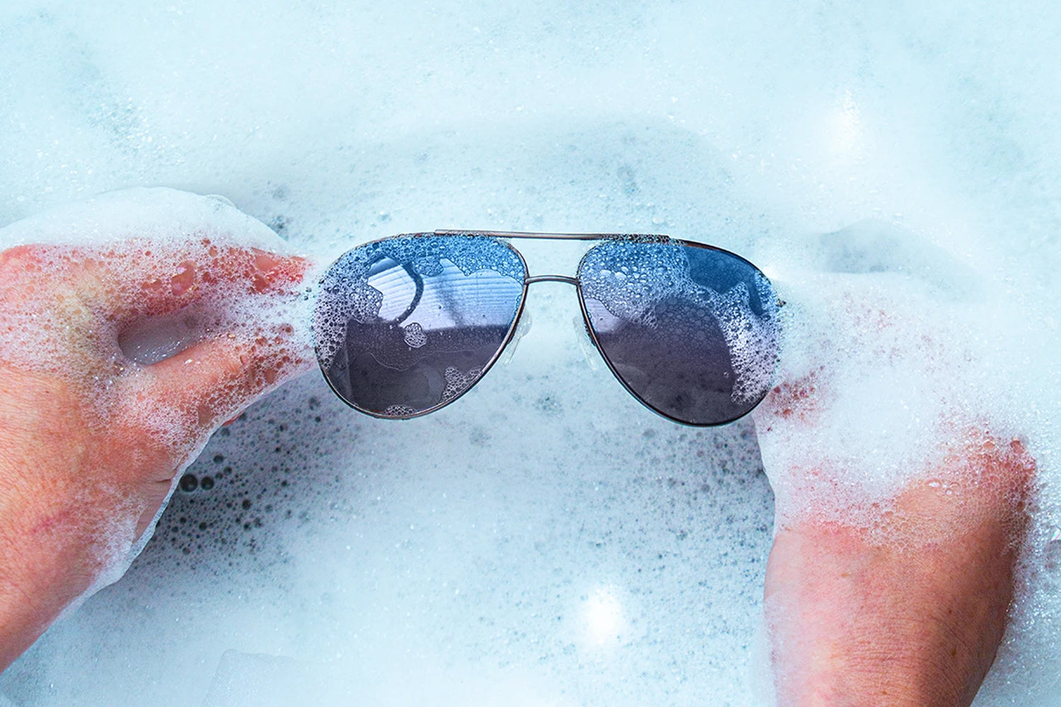 Washing EnChroma color blind glasses with soapy water, showing lens care and maintenance.